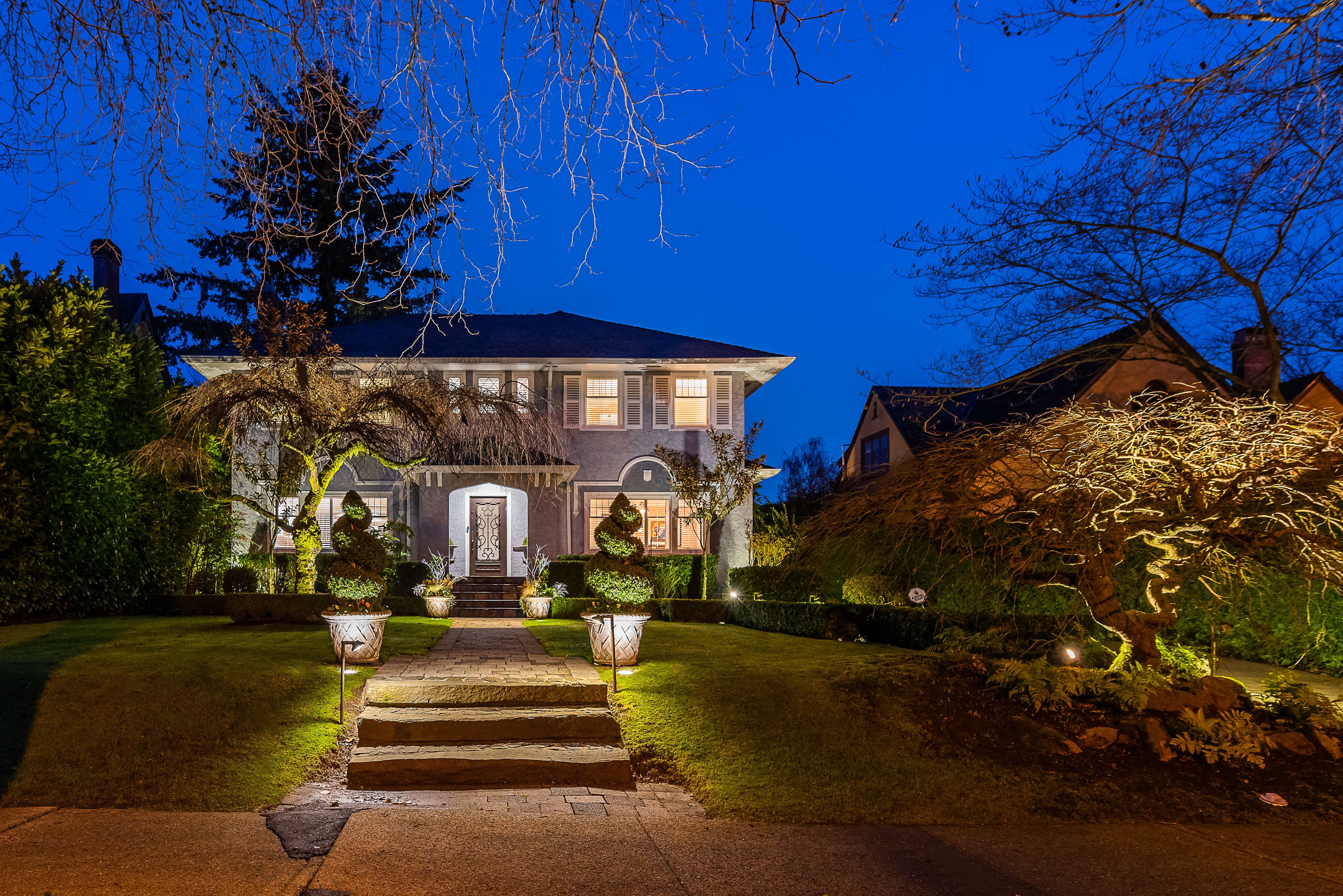 Elegant house with landscaped front yard and path, illuminated at night against a blue sky.