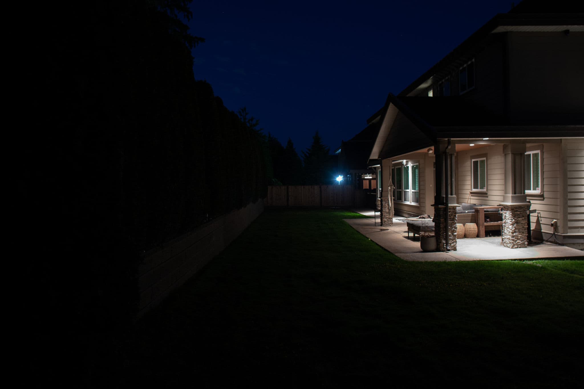 Nighttime exterior view of a house with outdoor lighting and lawn space.